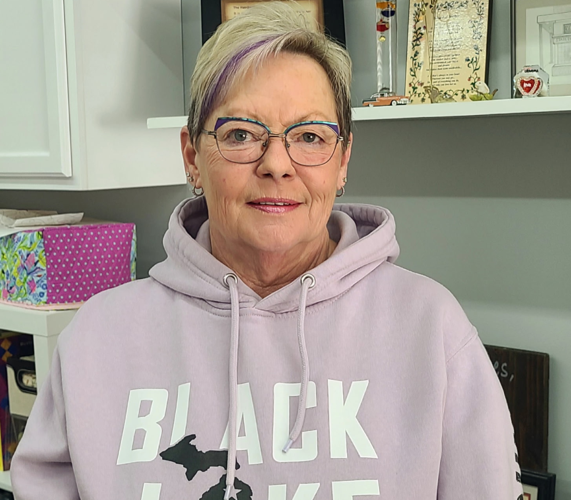 Smiling woman wearing glasses and a pink hoodie in a cozy room.