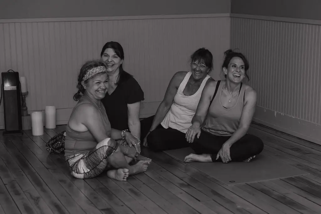 Four women sitting on a wooden floor smiling and posing for a photo.