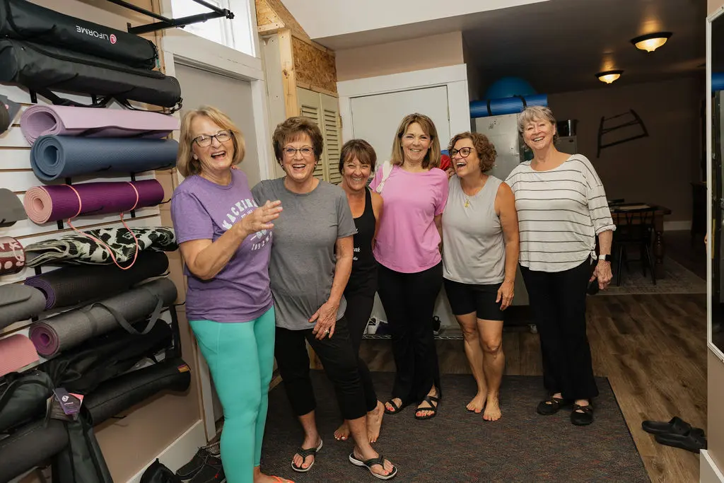 A group of six women smiling indoors, casually dressed.