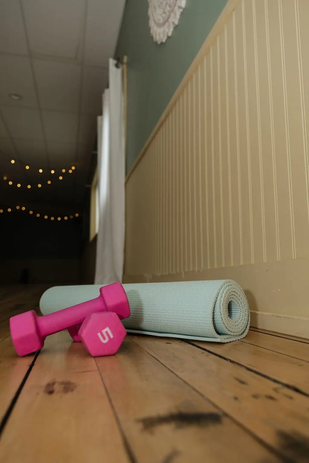 Pink dumbbells and a rolled yoga mat on a wooden floor.